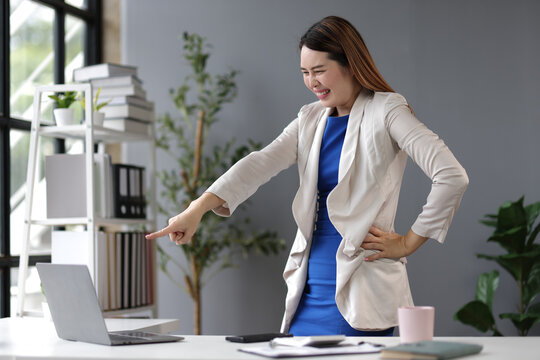 Asian businesswoman raising her arms in excitement while achieving a business target using her laptop in the office, expressing joy and accomplishment.