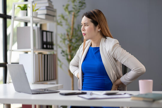 Businesswoman suffering back pain while working on laptop in office.