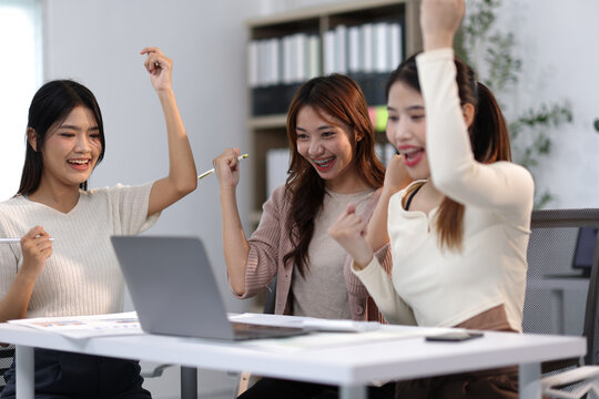 Excited businesswomen celebrating success while looking at laptop in office.