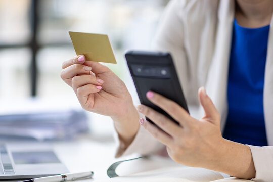Businesswoman using smartphone and credit card making online payment in office.