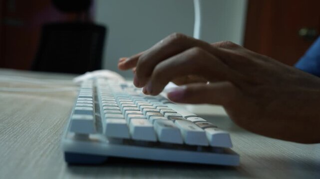 Hands typing on a white keyboard, Close-up of hands typing on a white computer keyboard at a wooden desk in a dim home or office workspace.