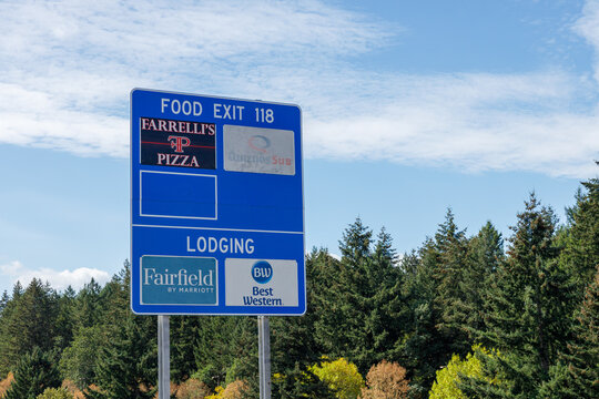 Blue I-5 Exit 118 sign lists Farrelli's Pizza, Quiznos Sub, Fairfield by Marriott, and Best Western against a backdrop of evergreen trees.