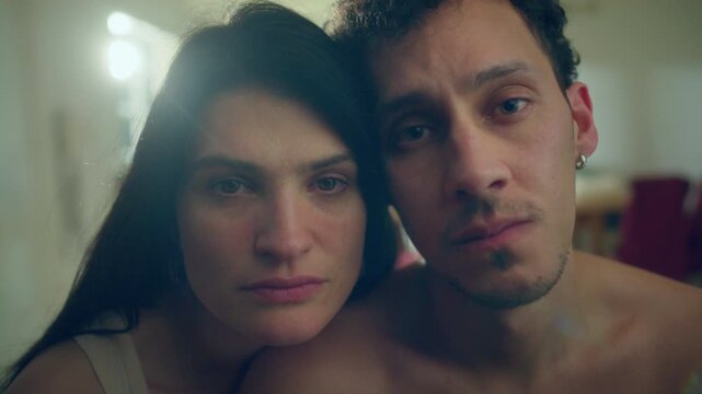Sad vulnerable young couple looking at camera with tearful eyes during difficult emotional moment in sunlit room at home. Close up, video portrait