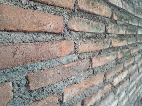 Close-up of a rustic red brick wall texture with rough cement mortar and subtle green moss accents.
