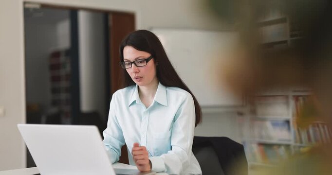 Focused adult businesswoman creating digital content on laptop at office workplace desk thinking aloud developing ideas planning tasks typing email brainstorming solutions and organizing work process
