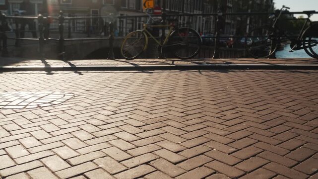 Low angle dynamic shot of people cycling on a sunny cobblestone street in Amsterdam city center, showcasing urban life and movement.