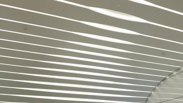 Modern architectural interior featuring parallel linear LED ceiling lights, clean white panels, and geometric reflections on a glossy wall surface.