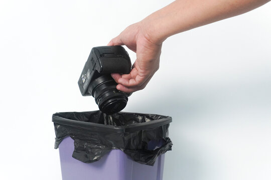 Hand throwing a digital camera into a trash bin against a white background with copy space