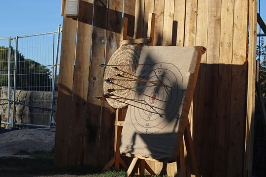 Straw archery target with arrows arranged at a medieval fair, set against a rustic wooden structure and used for traditional outdoor shooting activities, tournaments and historical recreation.