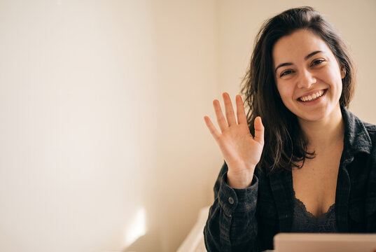 Young Caucasian woman waving hello at camera with friendly smile