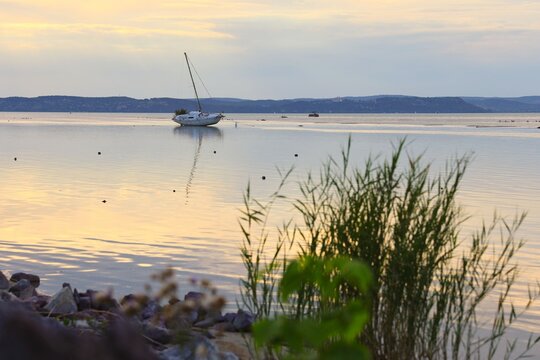 A peaceful sunset landscape at Lake Balaton in Hungary featuring a solitary sailboat resting on the ground due to low water levelsdrought, climate catastrophe.