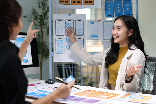 Asian woman creating user experience interface designs, discussing web application layouts and developing prototypes for digital products.