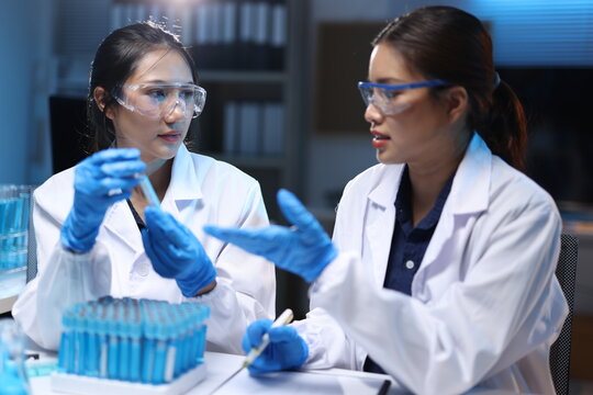 Woman scientists collaborating on research, holding test tube, analyzing results, and conducting experiments in a chemistry laboratory.