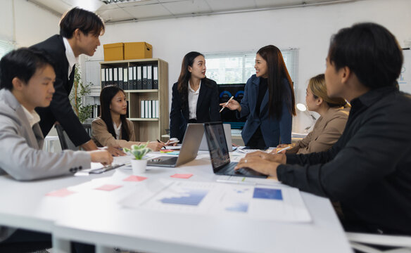 Asian business team collaborating on project strategy in office. Young Asian business professionals discussing ideas and analyzing data during a corporate meeting, teamwork and strategic planning.