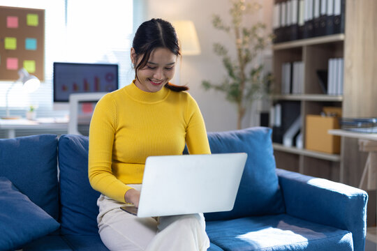 Asian woman working remotely from home. Young Asian woman smiling, sitting on the floor, using laptop for remote work or online studying at home.