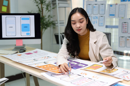 UX designer creating mobile application wireframes in office. Woman UX designer working on user interface wireframes at her office desk, developing a new mobile application.