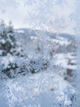 Intricate Frost Patterns on Window with Snowy Landscape Background.