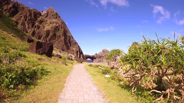 slow motion hand hold camera view look out to Lover's cave in Lanyu walking straight on the narrow pathway road to look out to the ocean with cliff at left side during good weather clear day with blue