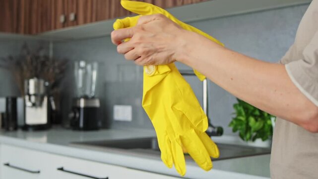 Hands stretch yellow cleaning gloves in kitchen, showing preparation for hygiene work. Protective handwear suits household chores, washing tasks, surface cleaning, and routine domestic care