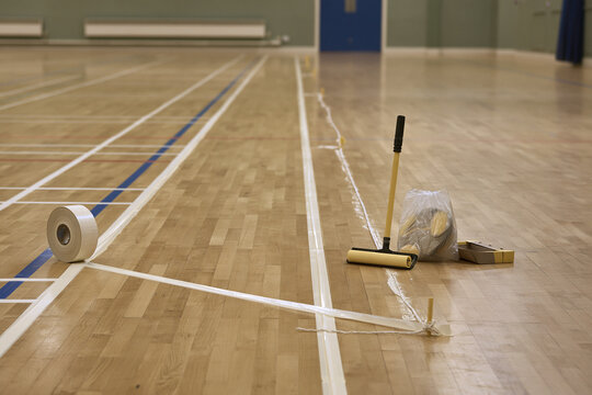Sports hall floor part marked with temporary court lines and a tape roll on the boards