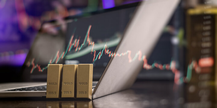 Digital wealth management. Gold bars resting on a computer with glowing forex and stock exchange trading data.