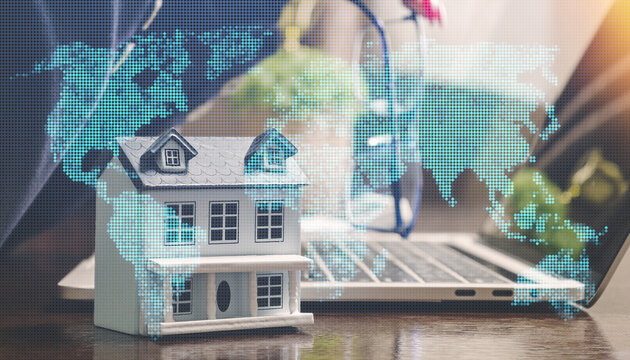 Global real estate investment concept. Miniature house with a digital world map overlay and a blurred laptop in the background.