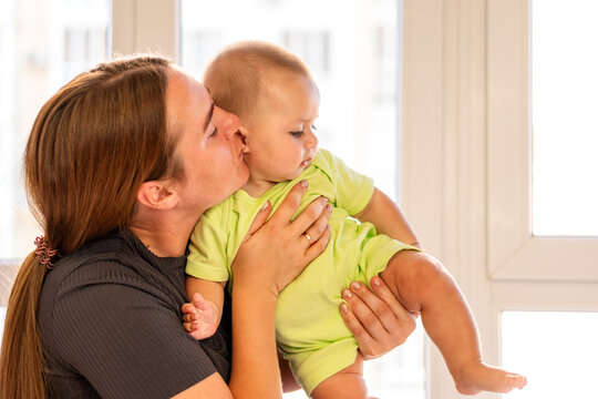 Mother Kisses Baby Boy While Holding Him Near Window