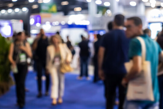 Defocused wide shot of a crowd of business people, executives, and visitors walking through a commercial exhibition pavilion aisle during a trade show convention event in Brazil.