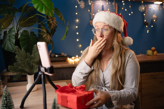 New Year, livestreaming, blogging and Merry Christmas. Upset woman blogger influencer in Santa hat shock negative bad news recording video blog using smartphone on tripod at home.