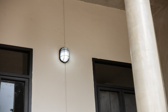Beige building facade with black window frame, hanging outdoor light, and round white column