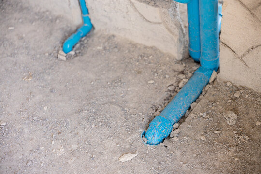 Blue metal pipe on dusty concrete floor with chipped paint, weathered surface, rough texture, and exposed construction detail in industrial setting