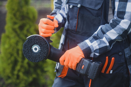 person holding angle grinder outdoors wearing orange gloves and black jacket for home improvement project in garden setting close-up practical and serene mood natural light clean background.