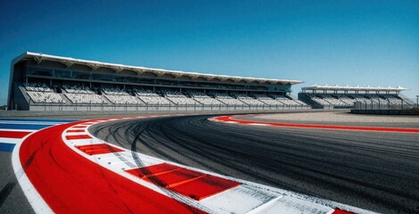 Obraz premium Empty asphalt race track with red, white curbs at sharp curve. Large grandstand stands under clear blue sky. Motorsport circuit features wide pavement, spectator seating for car racing competition.