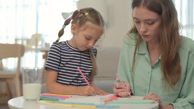 Mother and young daughter make Mother's Day card together at home, drawing and coloring side by side while enjoying creativity, learning, love, family bonding.