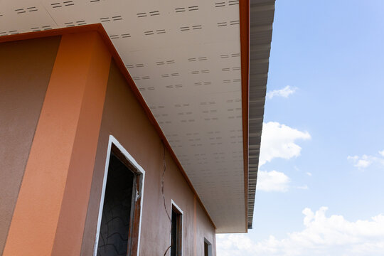 Orange stucco house wall with unfinished window openings and roof overhang beneath bright blue sky