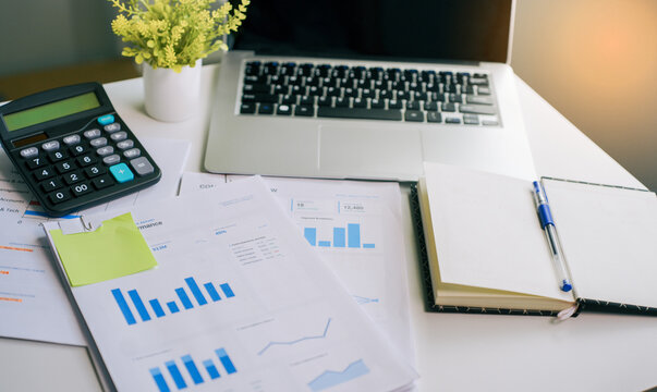 Financial analysis work desk featuring laptop computer calculator and business performance reports with charts for corporate planning