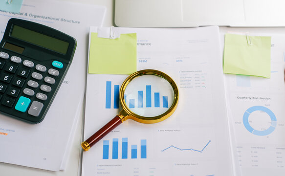 Financial analysis with magnifying glass on business data reports and calculator for corporate performance review and strategic investment planning