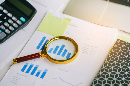 Financial analysis with magnifying glass over growth business performance chart report documents on office desk