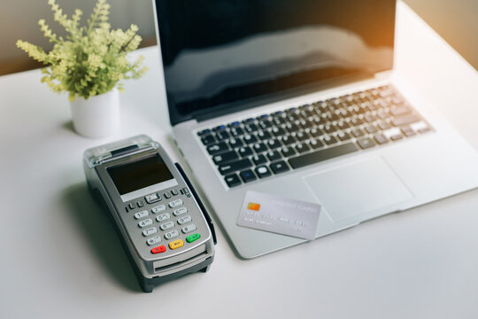 Credit card on laptop with point of sale terminal for electronic commerce and financial payment transaction on white desk