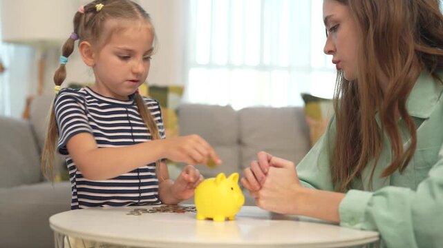 Mother teaches young daughter to save money using piggy bank at home, introducing financial education, saving habits, money management, parenting, life skills.