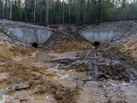 Drainage pipes set into concrete headwalls beside a muddy waterlogged ditch, with raw textures for civil engineering and flood control