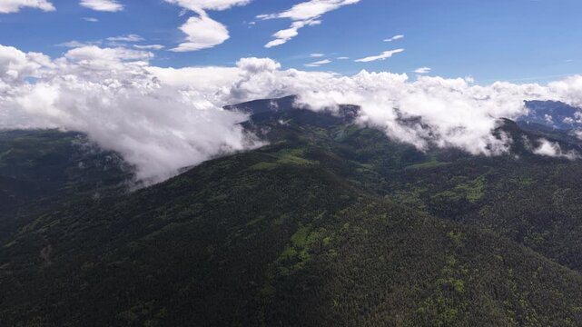 Aerial of mountainous landscape featuring dense forests and rolling low hanging clouds overlooking Carson National Forest in Taos County New Mexico