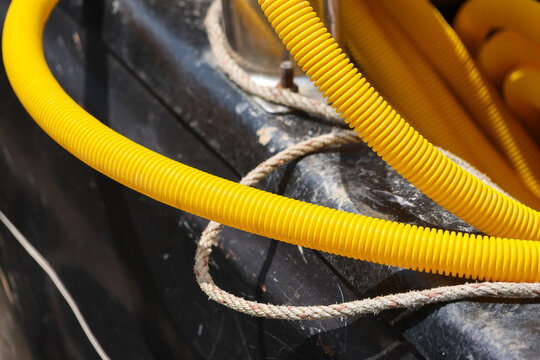 Yellow corrugated conduit and rope crossing weathered black surface create detailed industrial texture with contrast, wear, and tangled utility material in close view
