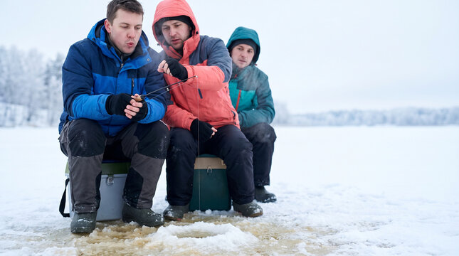 Group of friends fishing on a frozen lake during winter  