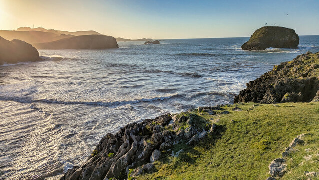 Sunset over Troenzo Beach with waves rolling onto golden sand, rocky headlands, and the Llubeces islet on the horizon. Celorio, Asturias, Spain