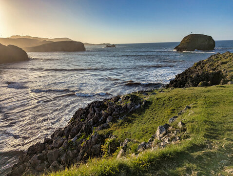 Sunset over Troenzo Beach with waves rolling onto golden sand, rocky headlands, and the Llubeces islet on the horizon. Celorio, Asturias, Spain
