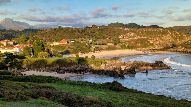 Elevated coastal view of Sorraos and Barro beaches with red-roofed houses, rocky headlands, and golden morning light over the Cantabrian Sea. Barro, Asturias, Spain