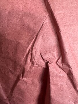 Crumpled dusty rose tissue paper with deep folds and creases