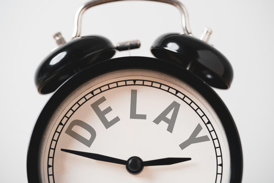 Delay concept with a close-up of a black vintage alarm clock displaying the word DELAY instead of numbers , it is symbolize missed deadlines, waiting time management and postponed plans schedule.