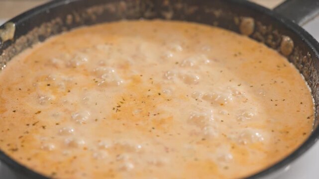 Tomato and garlic sauce with cream and spices bubbling and simmering in pan in home kitchen; process of making tomato pasta; preparation of delicious and healthy Italian meal; food closeup